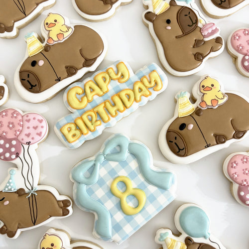 Birthday cookies: capybaras in party hats with ducklings, a CAPY BIRTHDAY plaque, balloons and a gingham number eight