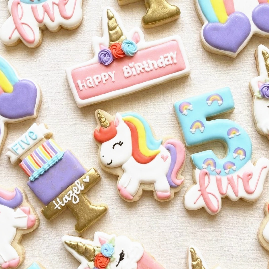 Unicorn birthday cookies: a rainbow-maned unicorn, happy birthday plaque, number cookie and layered cake in pastels and gold